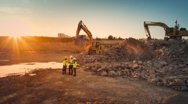 Aerial Drone Shot Of Construction Site With Excavators On Sunny Day: Diverse Team of Real Estate Developers Discussing Project. Civil Engineer, Architect, Inspector Talking And Using Tablet Computer.